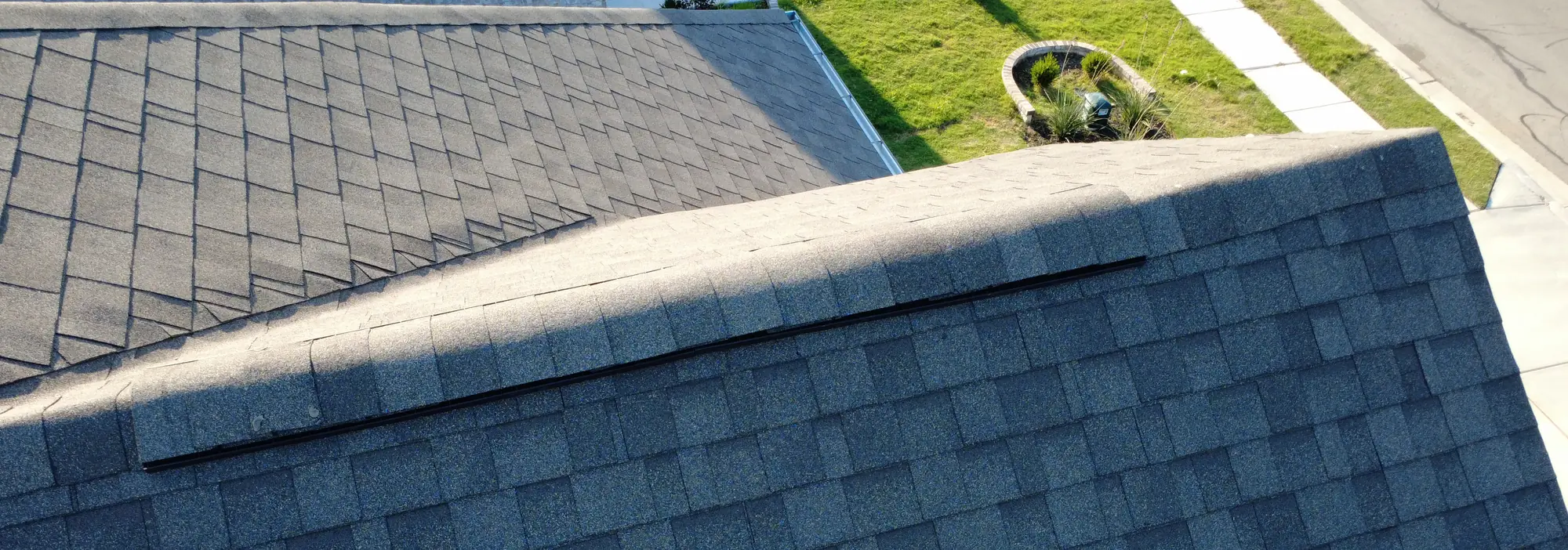 An aerial view along a sunlit roof ridge, with the front lawn, walk and street beyond it