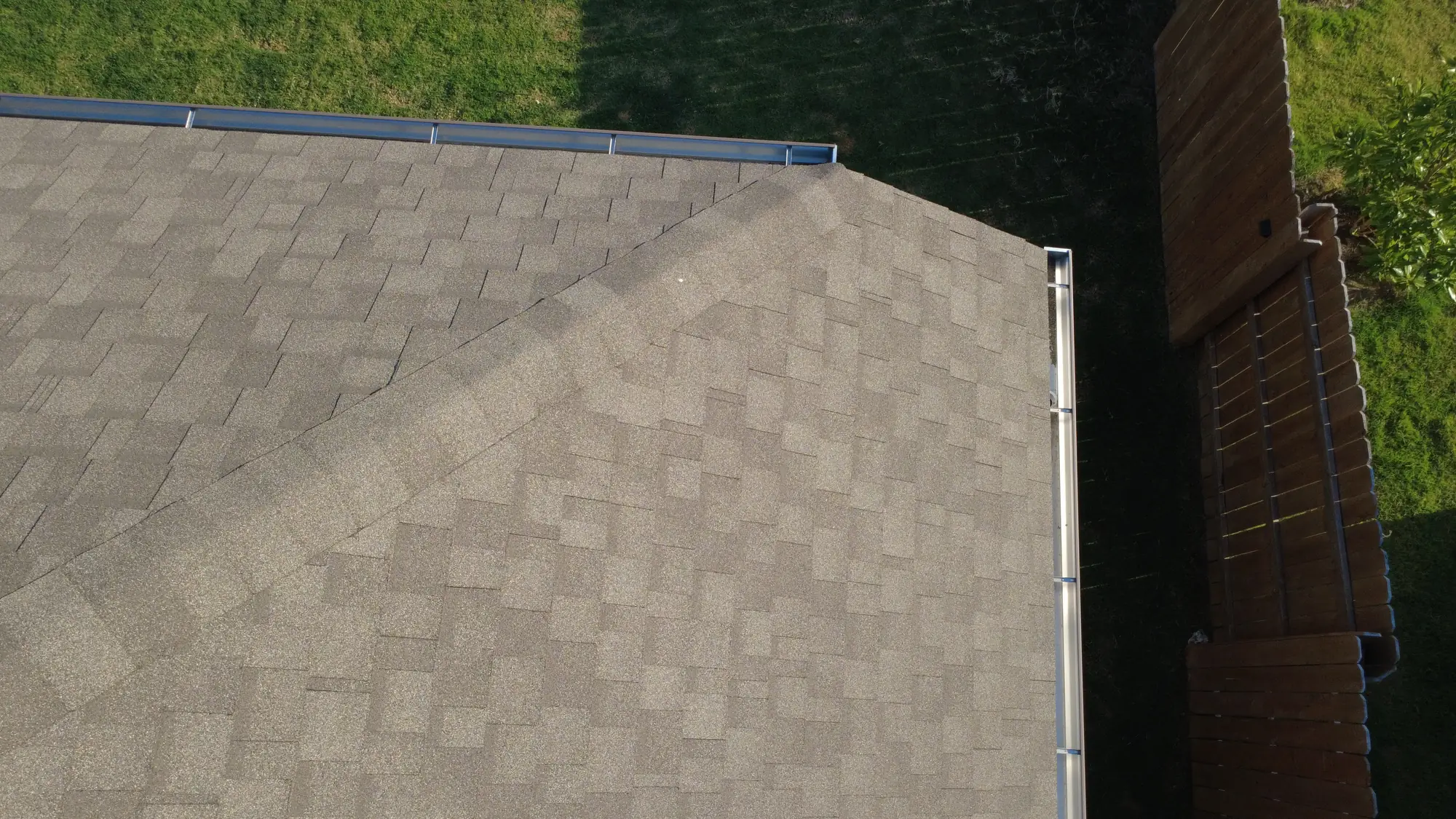 A shingled hip roof photographed from directly above at golden hour, with the back lawn and fence beside it